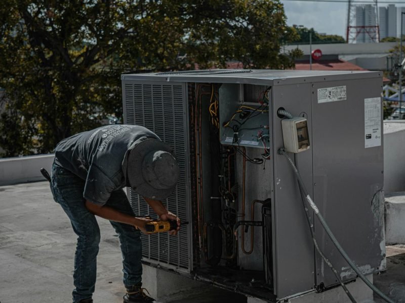 A technician is repairing an air conditioning unit on a rooftop, demonstrating skilled manual work.
